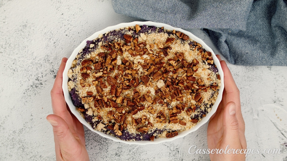 sweet potato casserole topped with sugar mixture and pecans held by two hands before baking