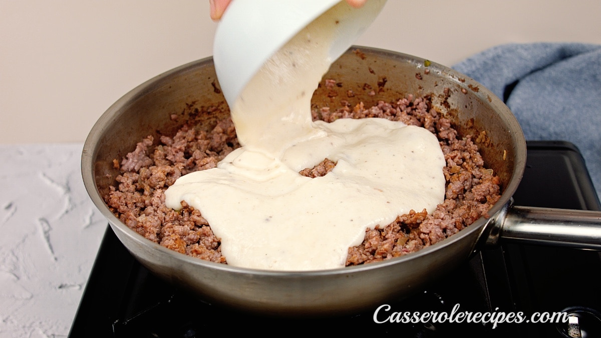 pouring white sauce over the ground beef