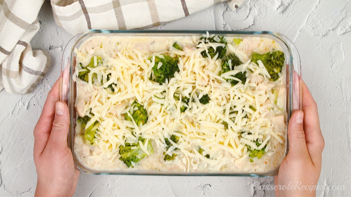 broccoli and chicken casserole held by two hands before baking