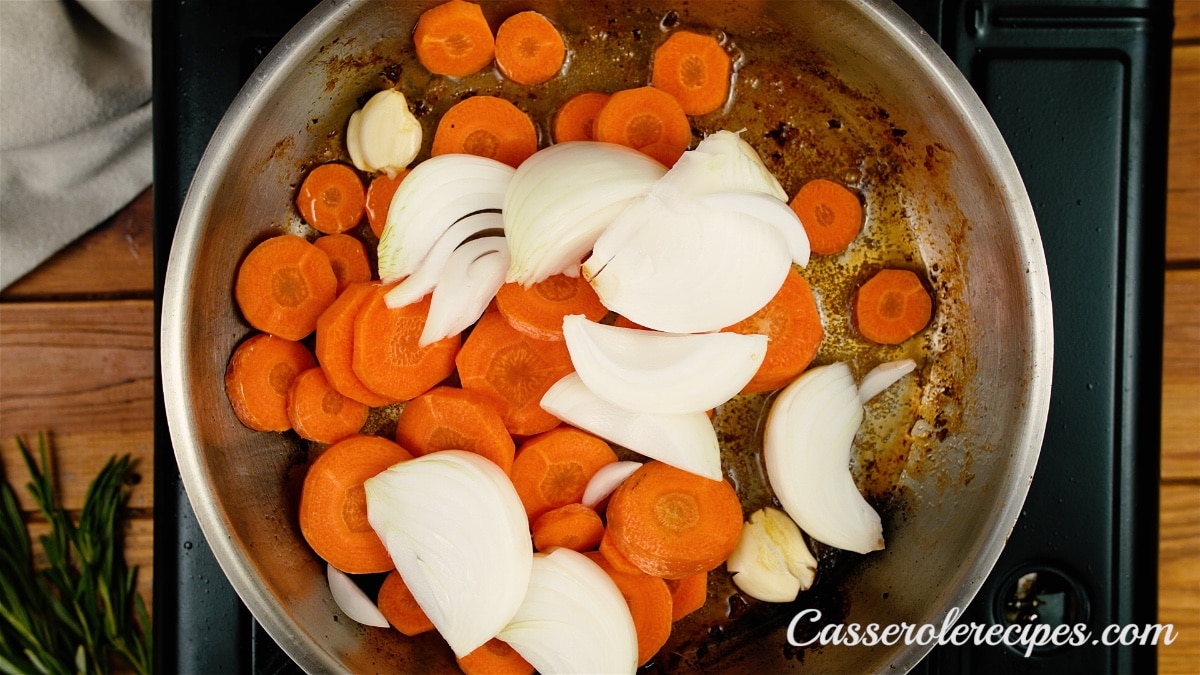 sliced carrots and garlic cloves and sliced onions added to pan