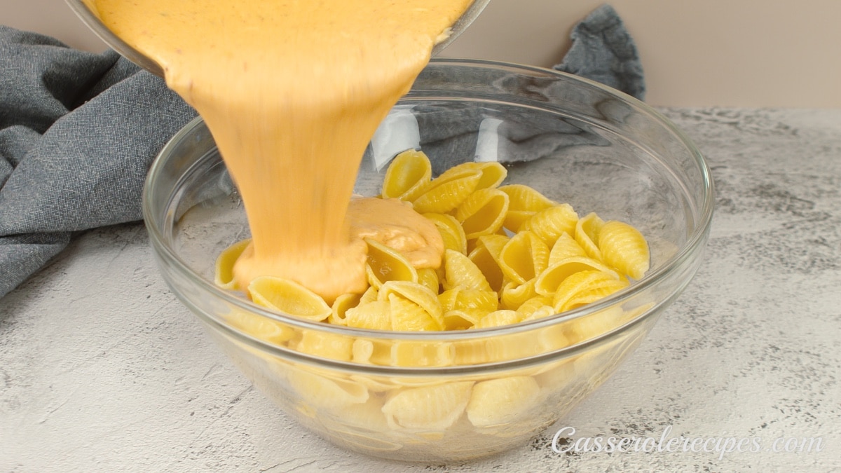 pouring cheese sauce over cooked shell pasta