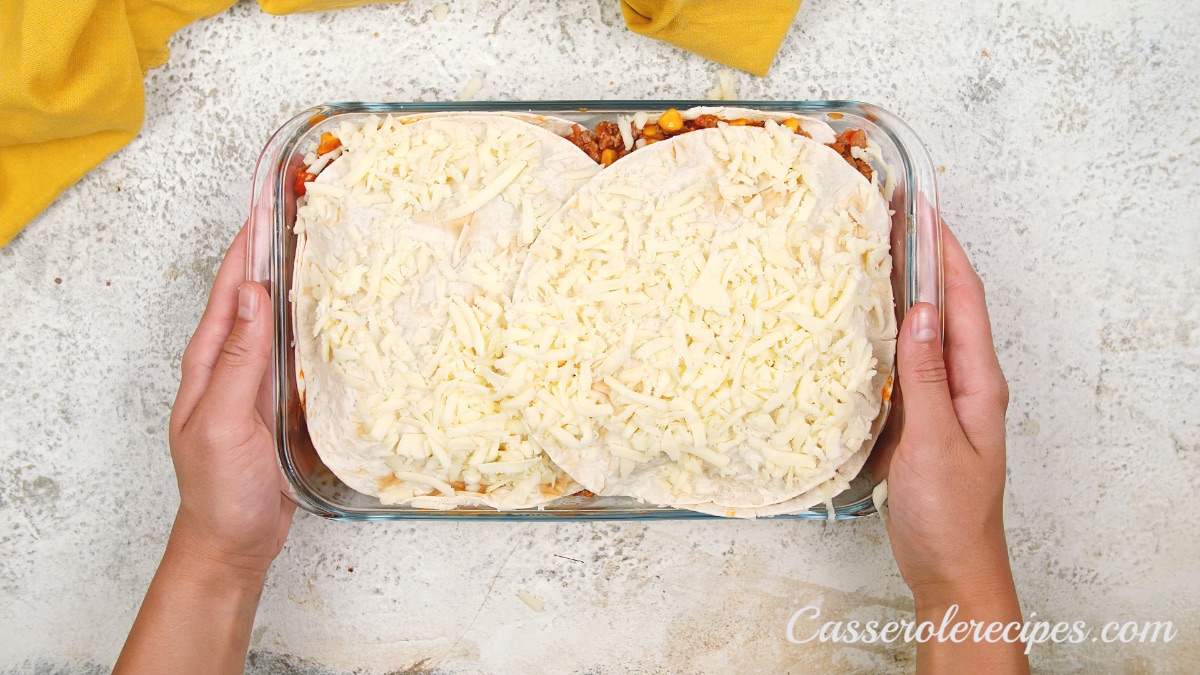 cheese sprinkled on top of tortillas and baking dish held by two hands