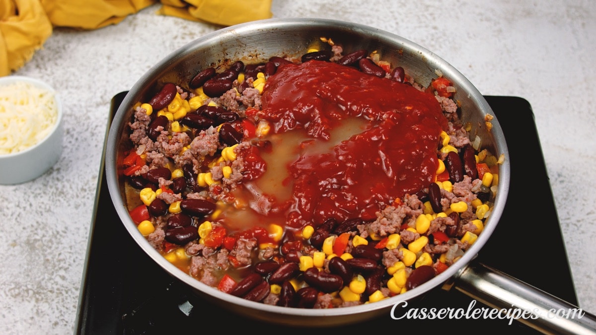 sauce on top of beans, corn, and meat in a pan