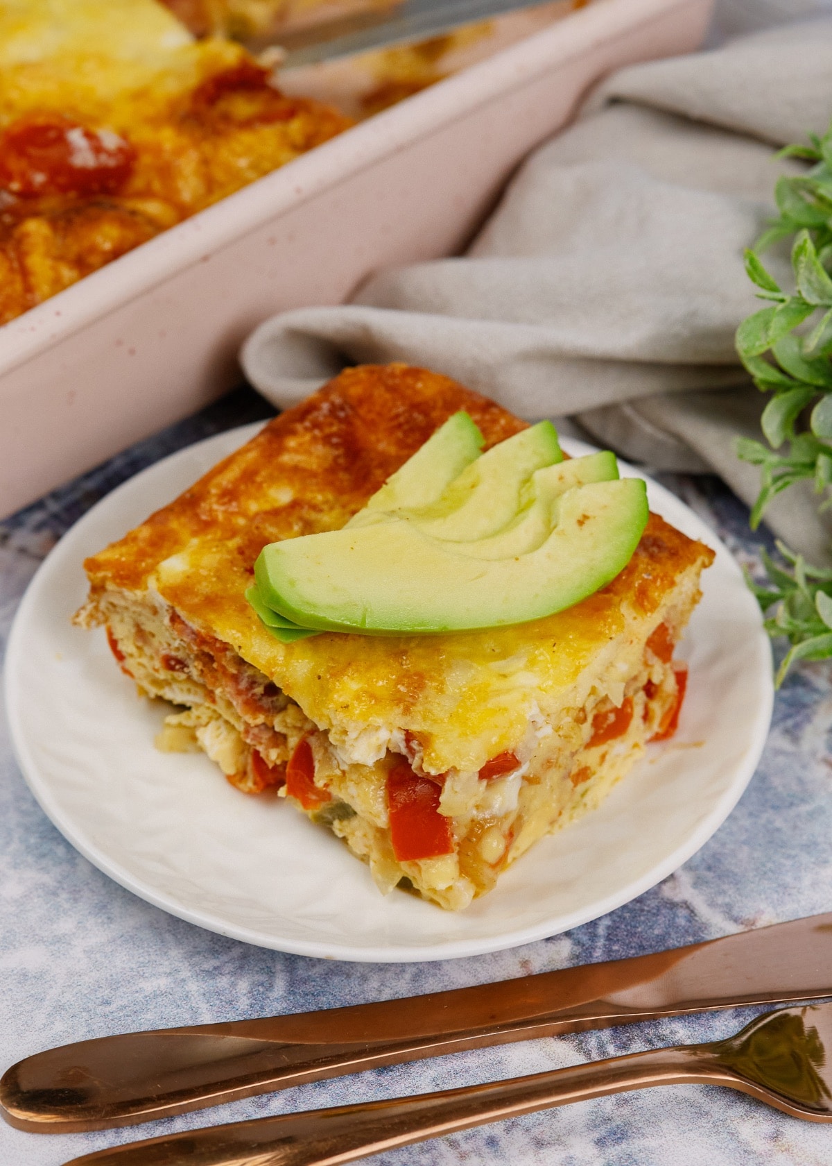 a slice of breakfast casserole on a white plate with a slice of avocado on top