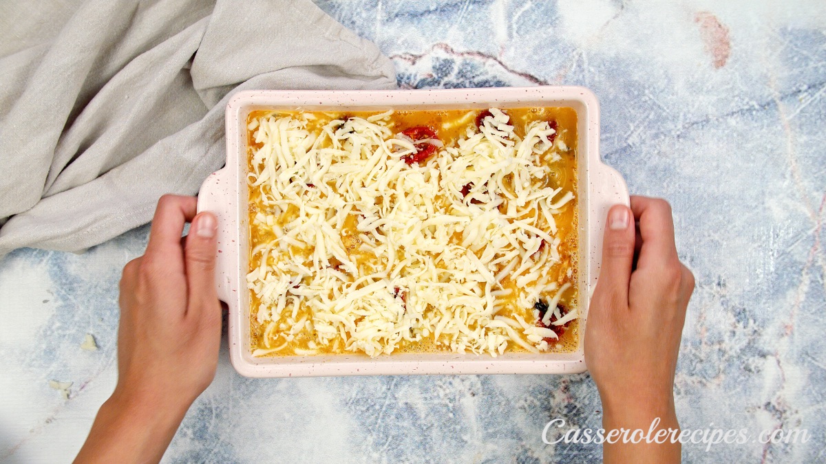 shredded cheese on top of casserole in a white baking dish held by two hands