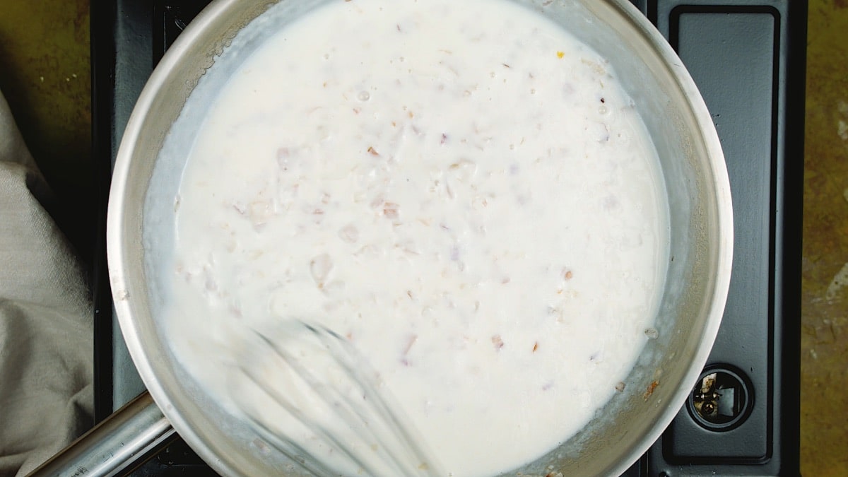a whisk over a creamy sauce in a pan