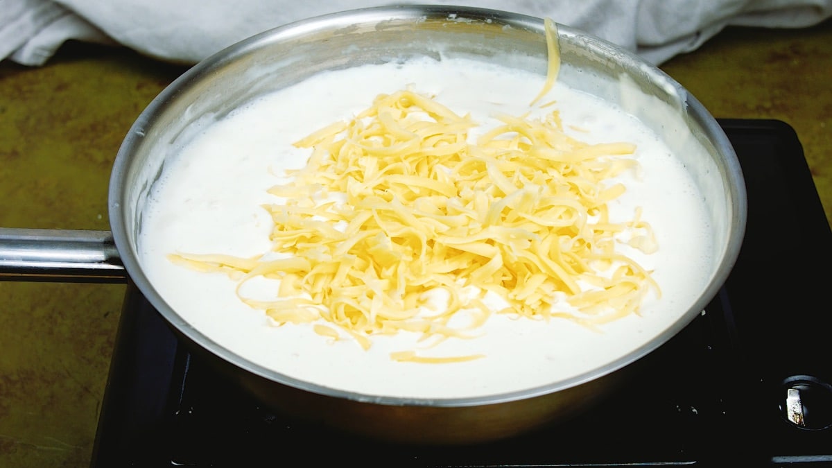shredded cheese on top of a white sauce in a pan