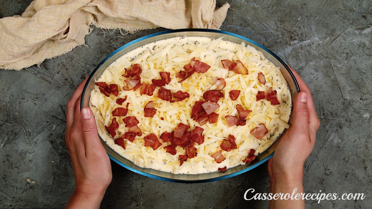 bacon sprinkled over casserole in a baking dish being held by two hands