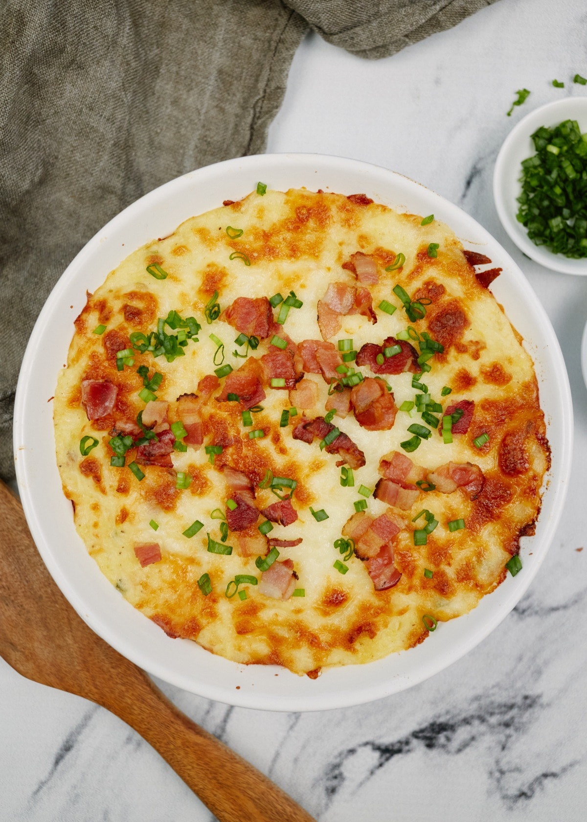 twice baked potato casserole in a baking dish topped with bacon and chives