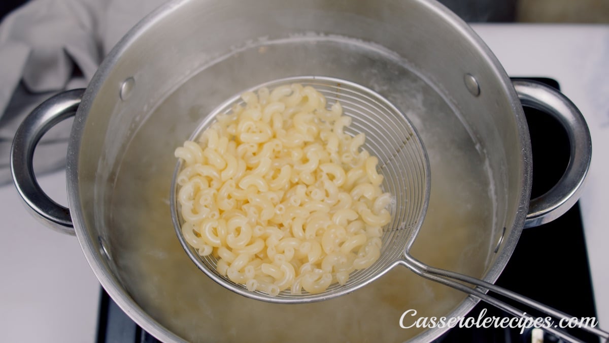 lifting cooked macaroni out of a pot of water with a sieve