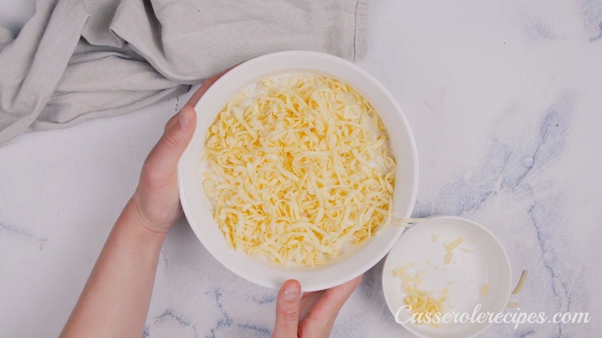 sprinkling shredded cheese over macaroni in a baking dish