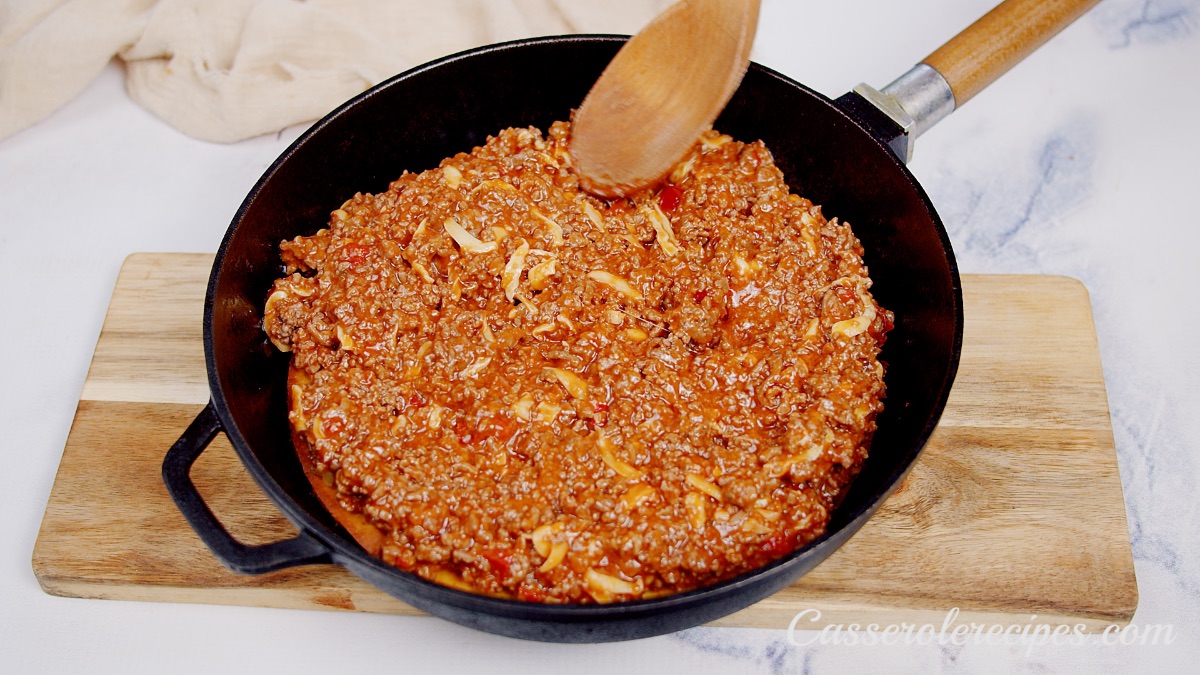 stirring ground beef mixture with a wooden spoon in a cast iron pan