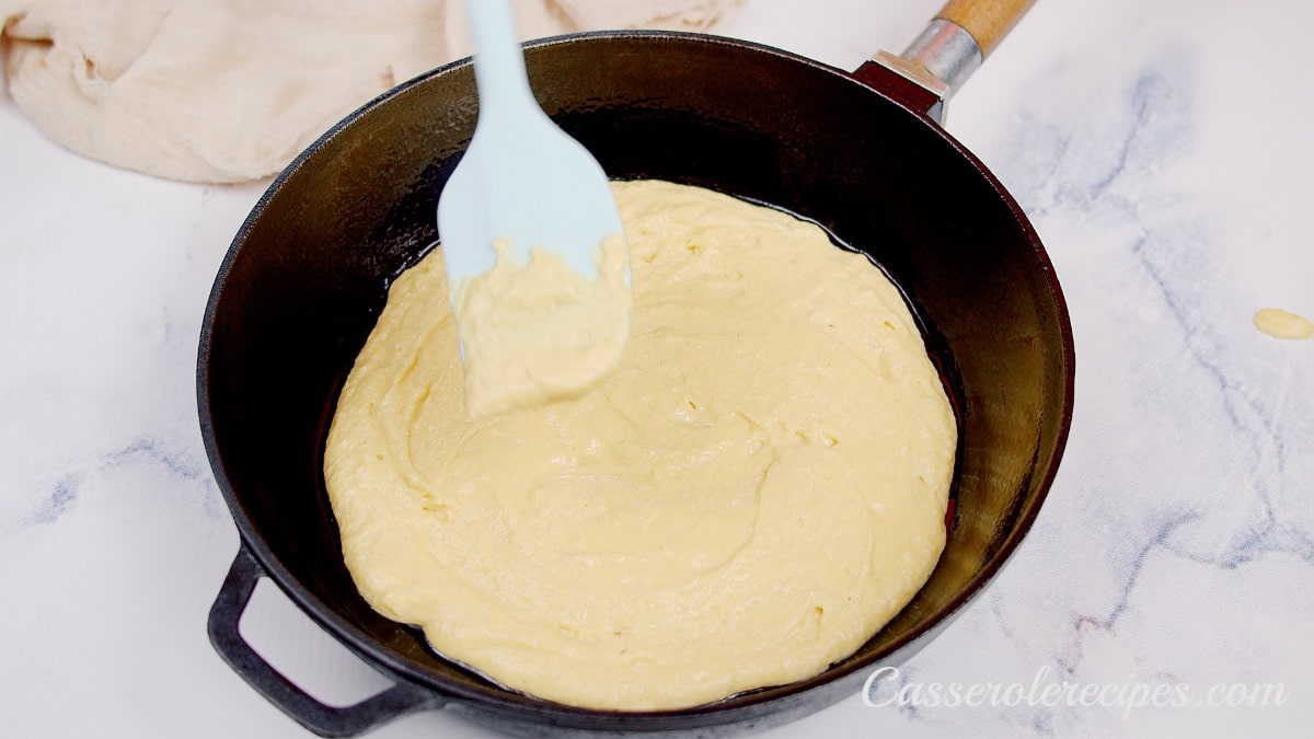 spreading buttermilk mixture in a cast iron skillet with a white spatula