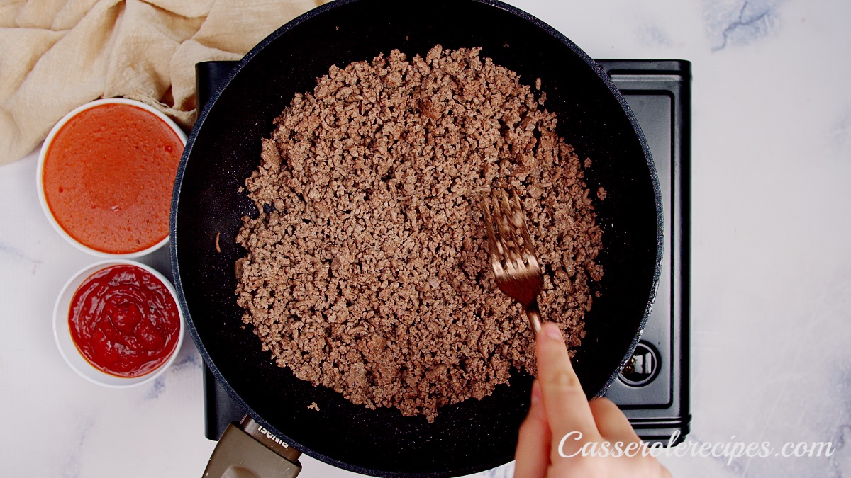 stirring browned ground beef with a fork in a cast iron pan