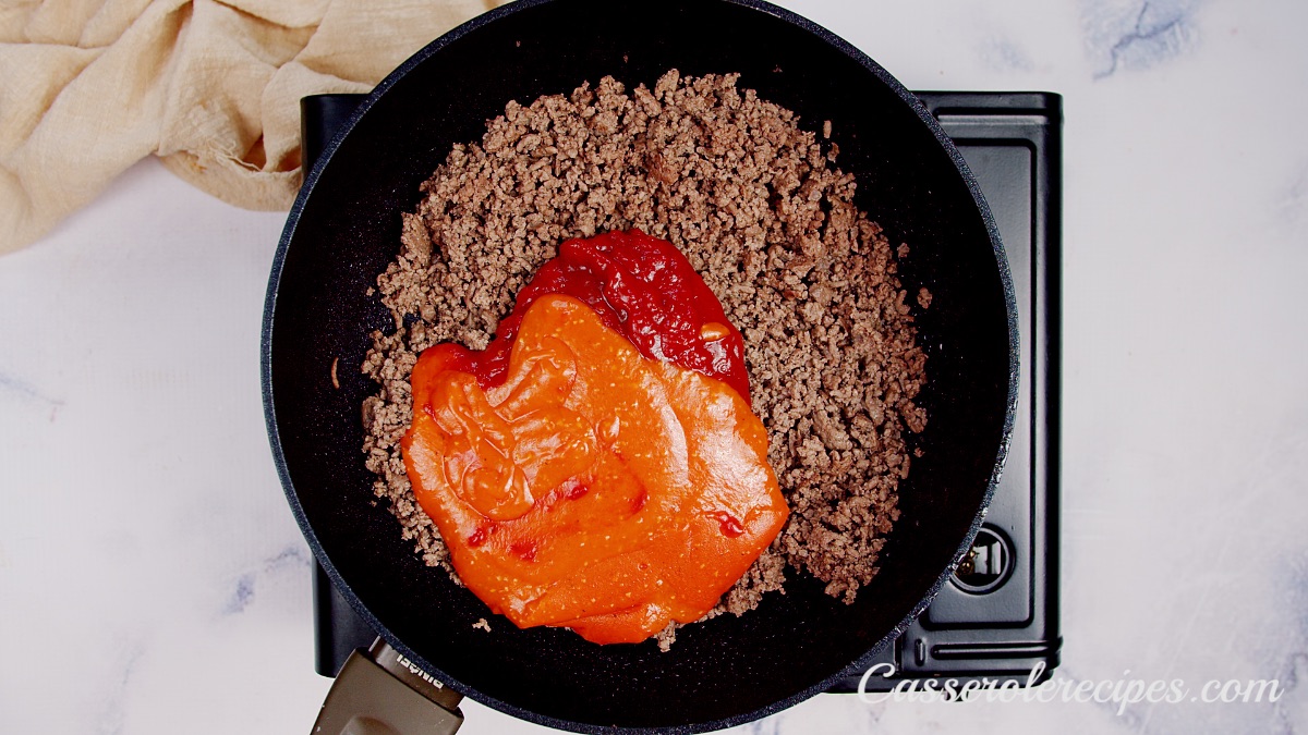 tomato sauce and enchilada sauce poured into cooked ground beef in pan