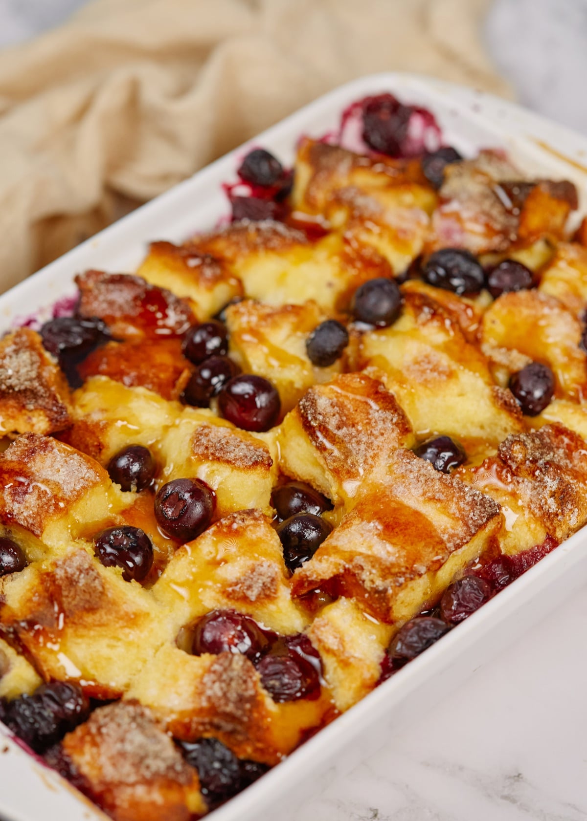 baked blueberry french toast casserole in a white baking dish on a wooden board