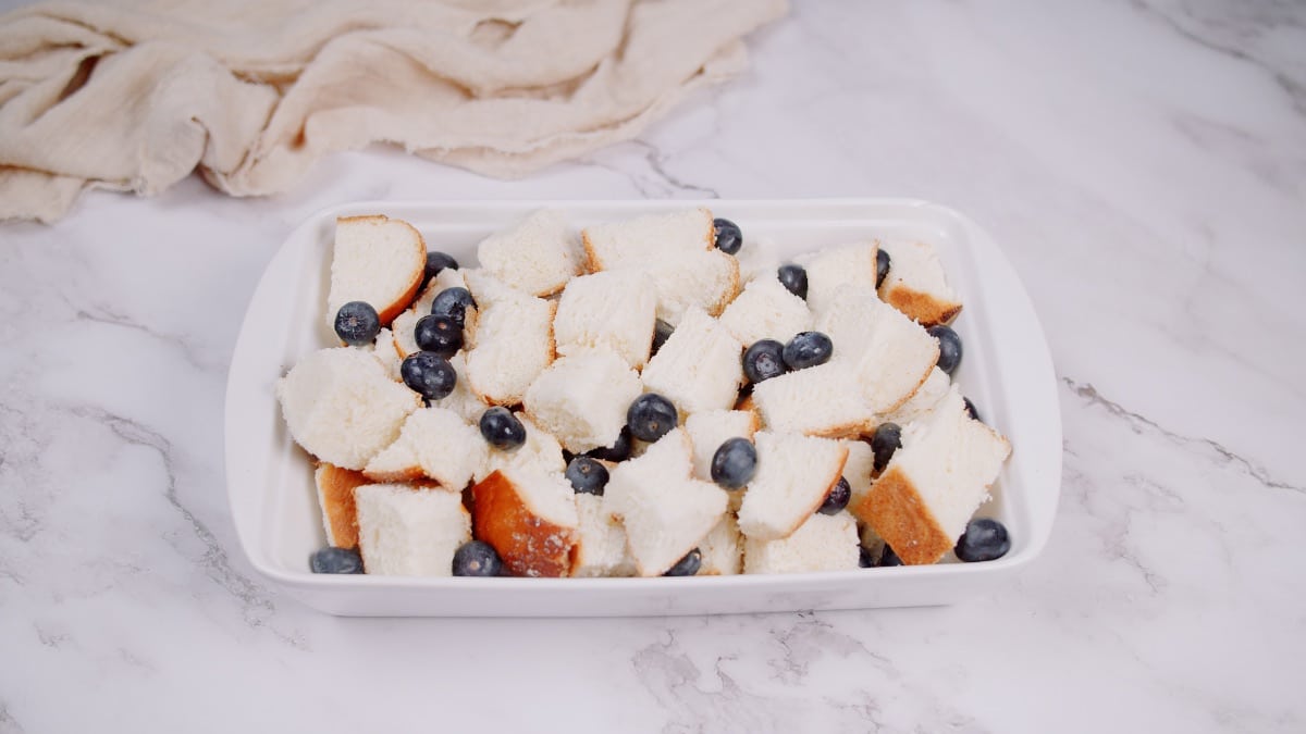 bread cubes and blueberries in a white baking dish