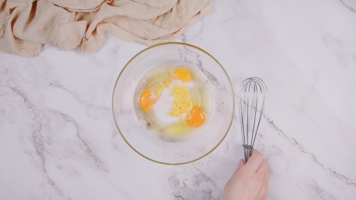 a hand holding the whisk beside the glass bowl with eggs and milk