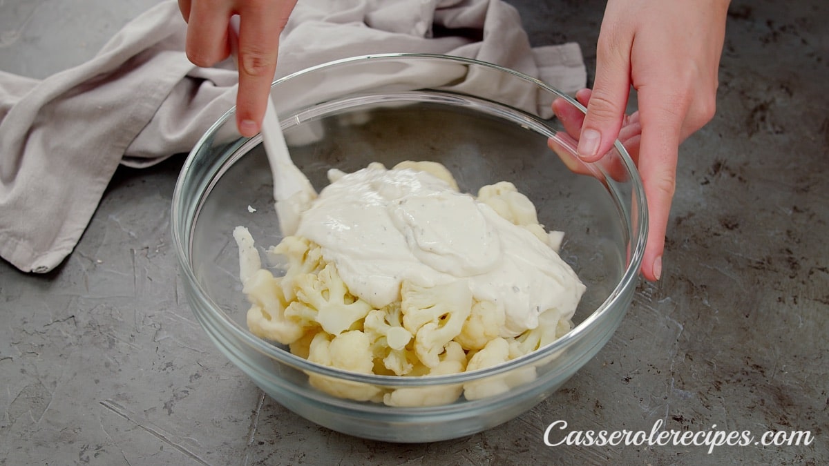 mixing cauliflower and sauce with a white spatula