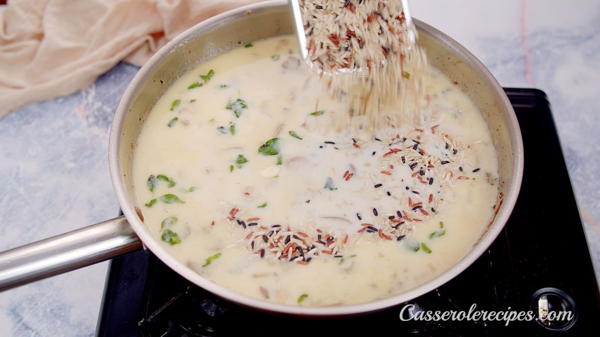 Sprinkling rice into pan with stock, cream, and mushrooms