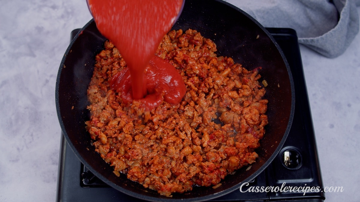 pouring tomato sauce over sausage in pan