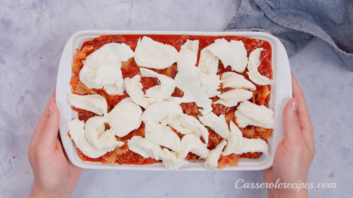 two hands holding baking dish with torn mozzarella on top
