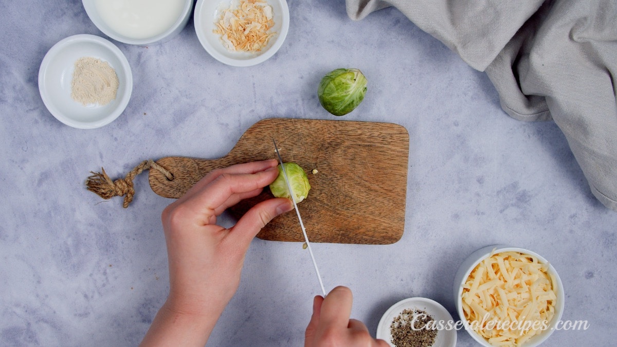 two hands cutting a brussel sprout on a wooden cutting board