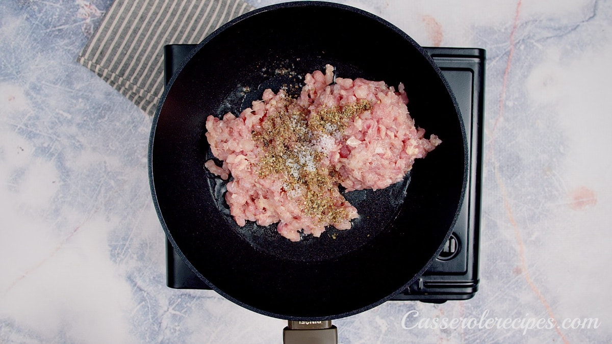raw ground chicken and spices in a cast iron pan
