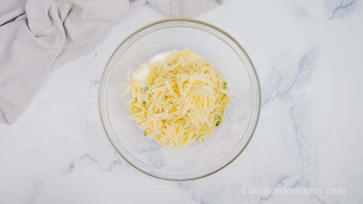 shredded cheese on top of sour cream in glass bowl