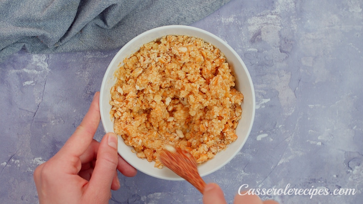 mixing butter and crackers in a small white bowl with a wooden spoon