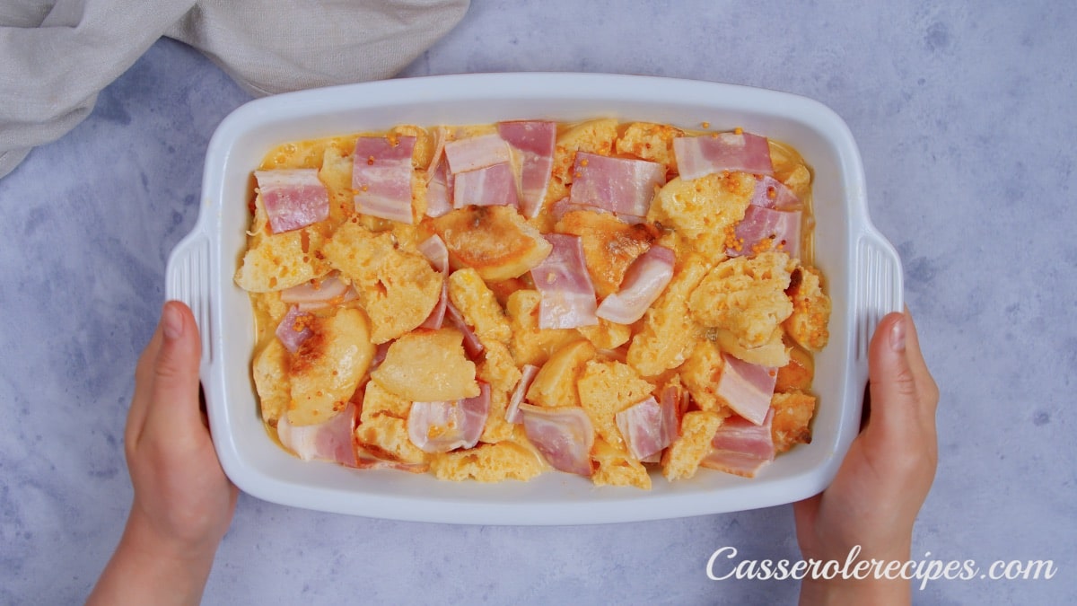 two hands holding eggs benedict casserole before baking