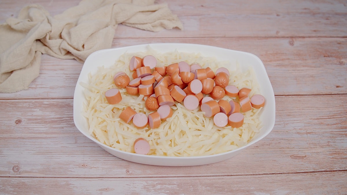 hashbrowns topped with chopped hot dogs in a white baking dish