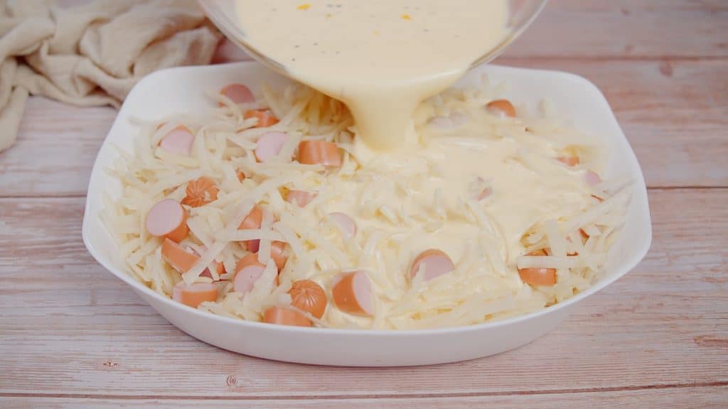 pouring cream mixture over hot dog casserole