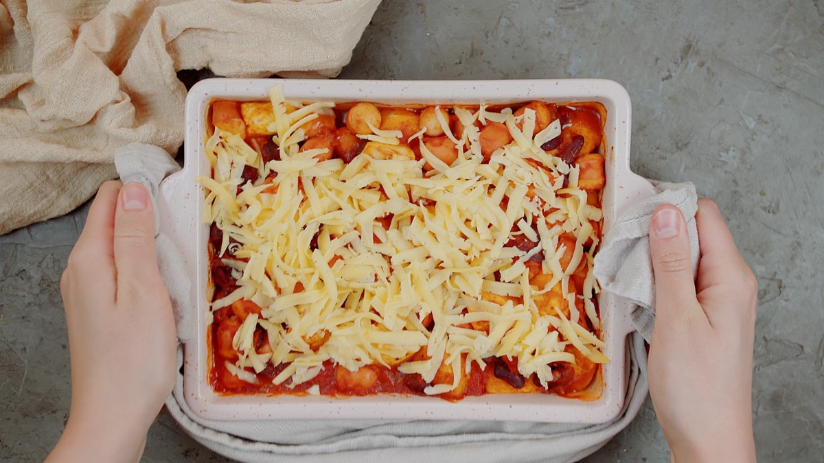 two hands holding Mexican biscuit casserole topped with shredded cheese