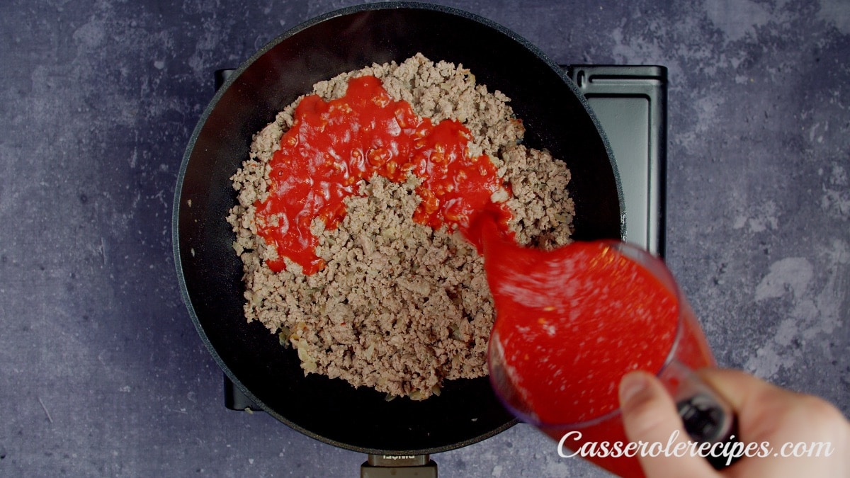 pouring tomato sauce over cooked ground sausage