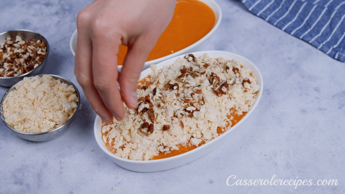 a hand sprinkling chopped pecan over baking dish