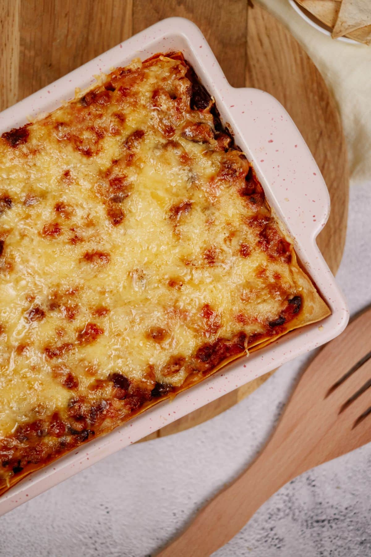 rectangular white casserole dish filled and topped with cheese laying by wooden spoon