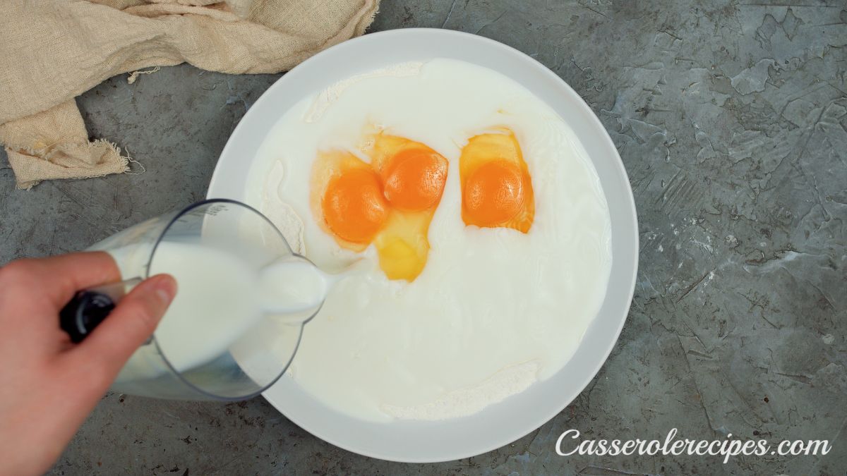 milk being poured into bisquick and egg mixture in white bowl