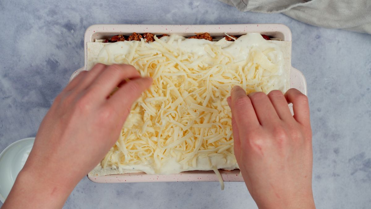 hands sprinkling cheese on top of burrito casserole before baking