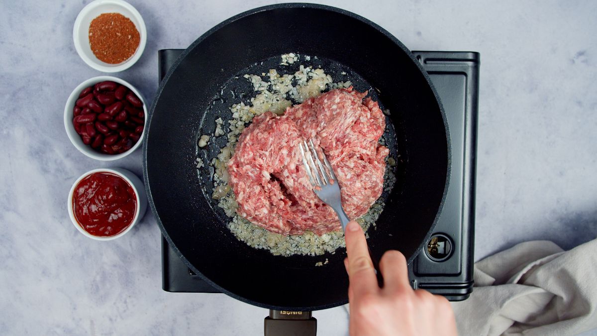 fork being used to break up ground beef in skillet