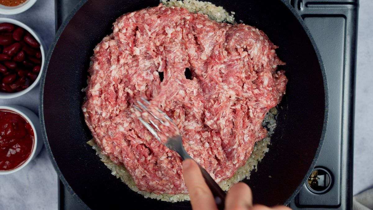 fork breaking up ground beef in skillet as it cooks