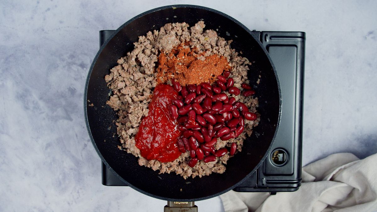 cooked ground beef in skillet topped with sauce, beans,a nd spices