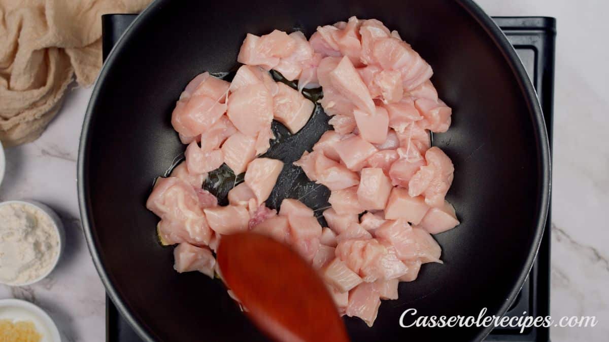 red spoon stirring raw chicken pieces in black skillet