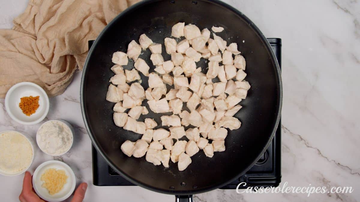 cooked chicken pieces in large black skillet on hot plate on marble table