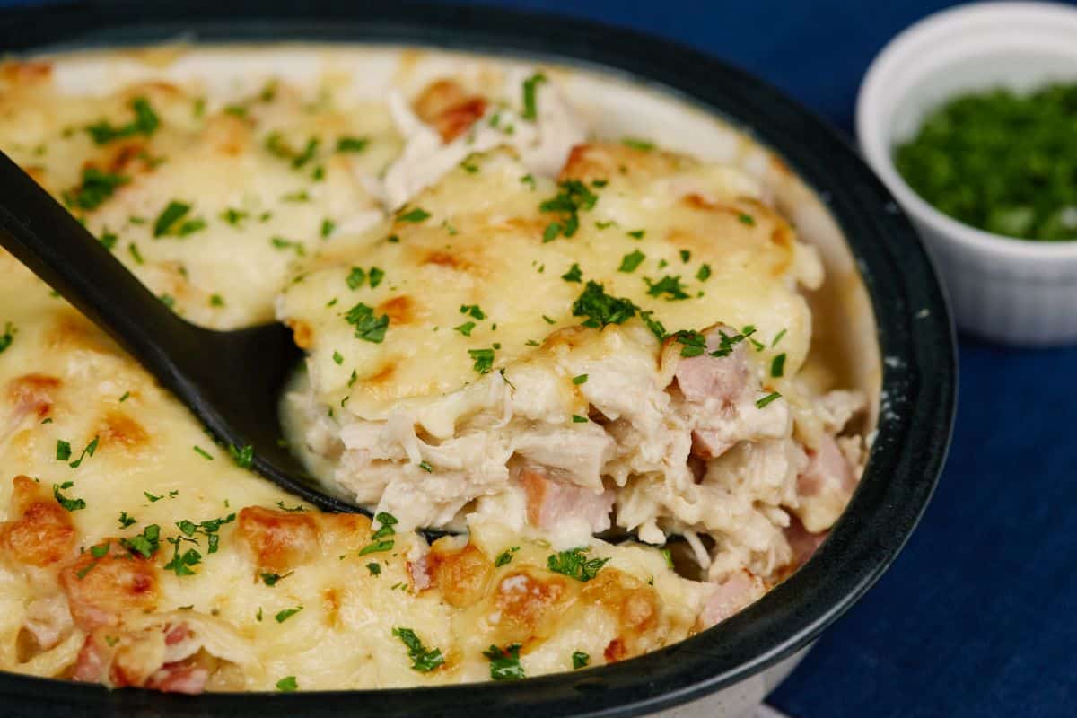 black spoon holding chicken cordon bleu casserole above dish