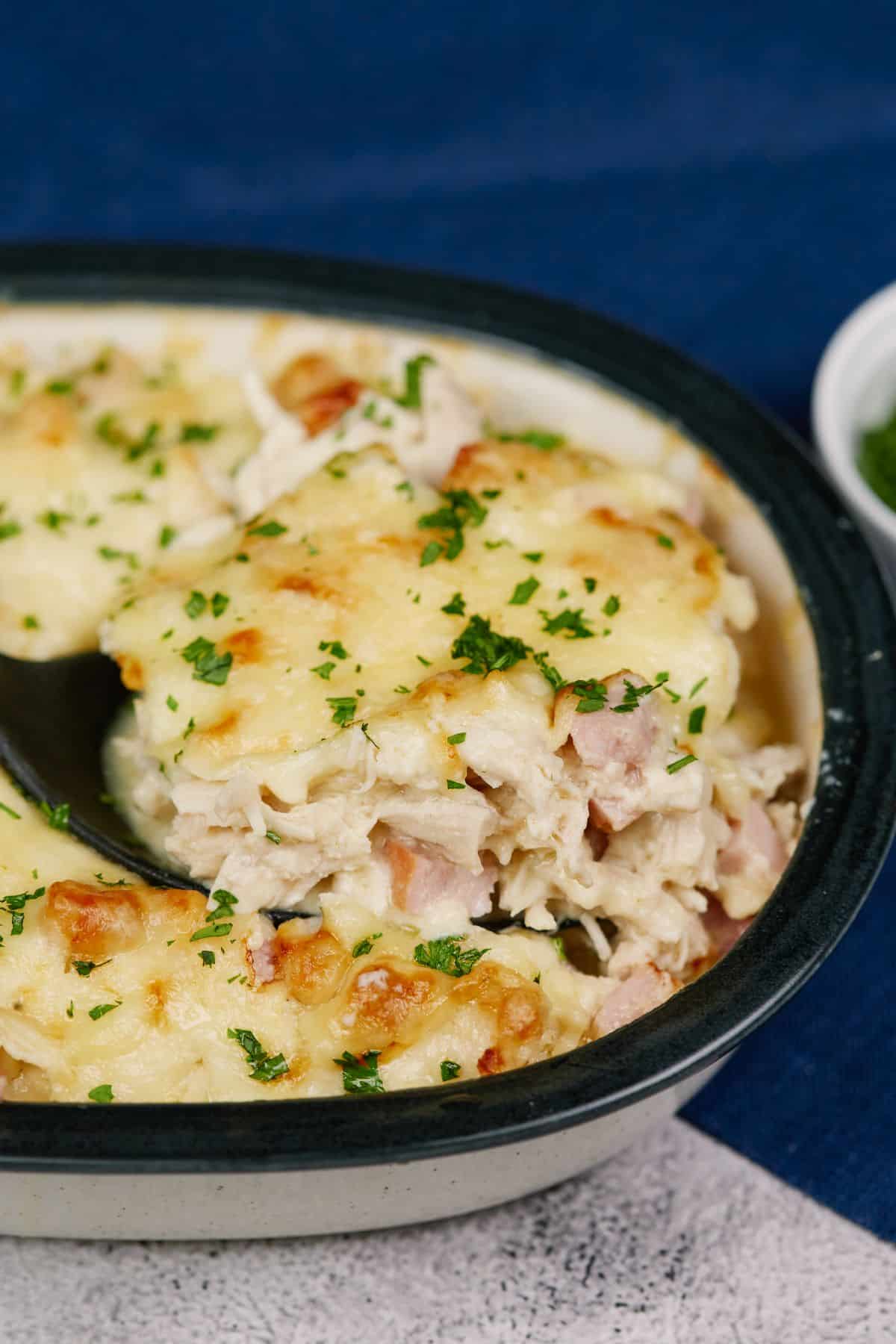 black rimmed casserole dish of chicken cordon blue with black spoon