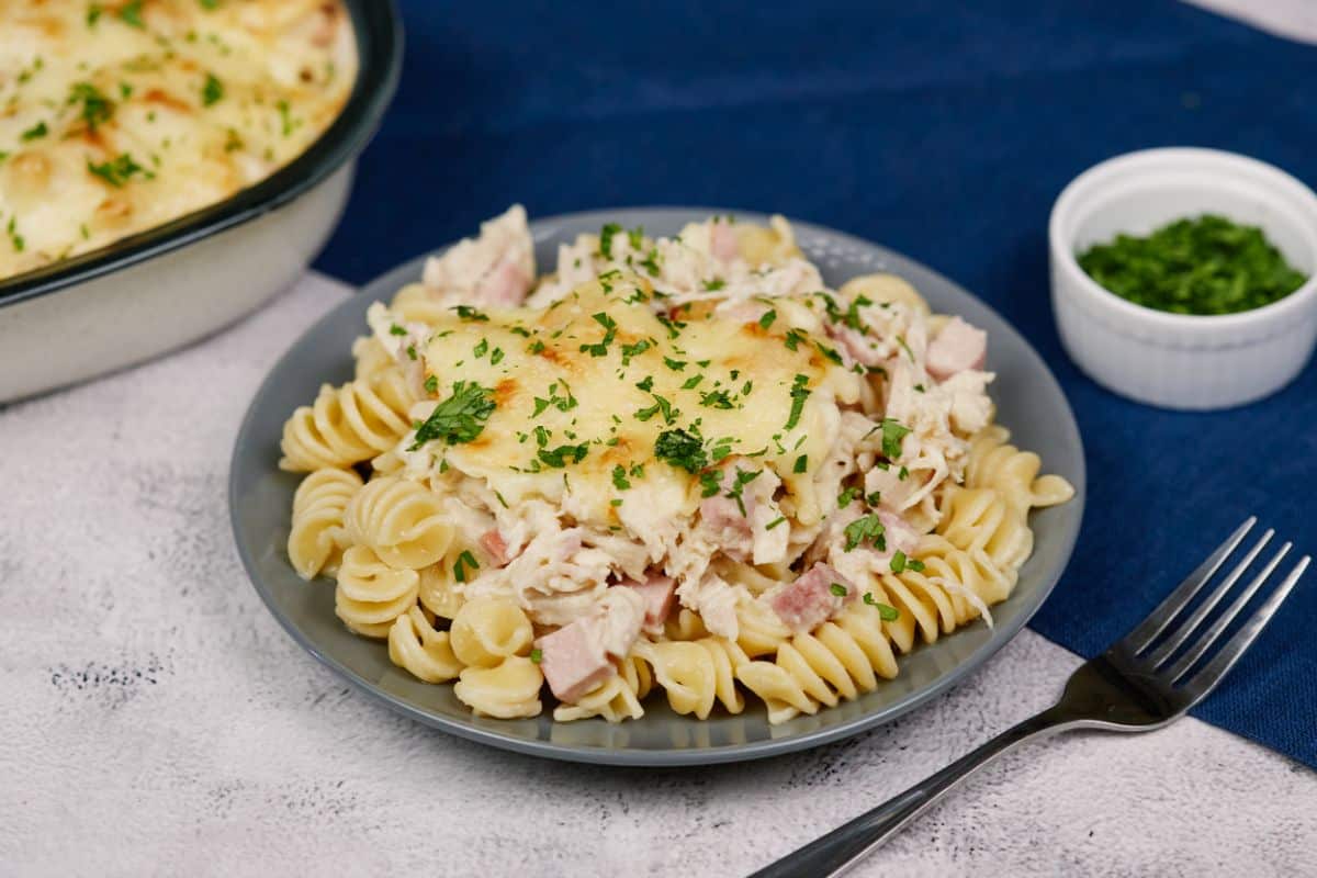 round gray plate of pasta and chicken cordon bleu casserole sitting on table with blue and white tablecloth