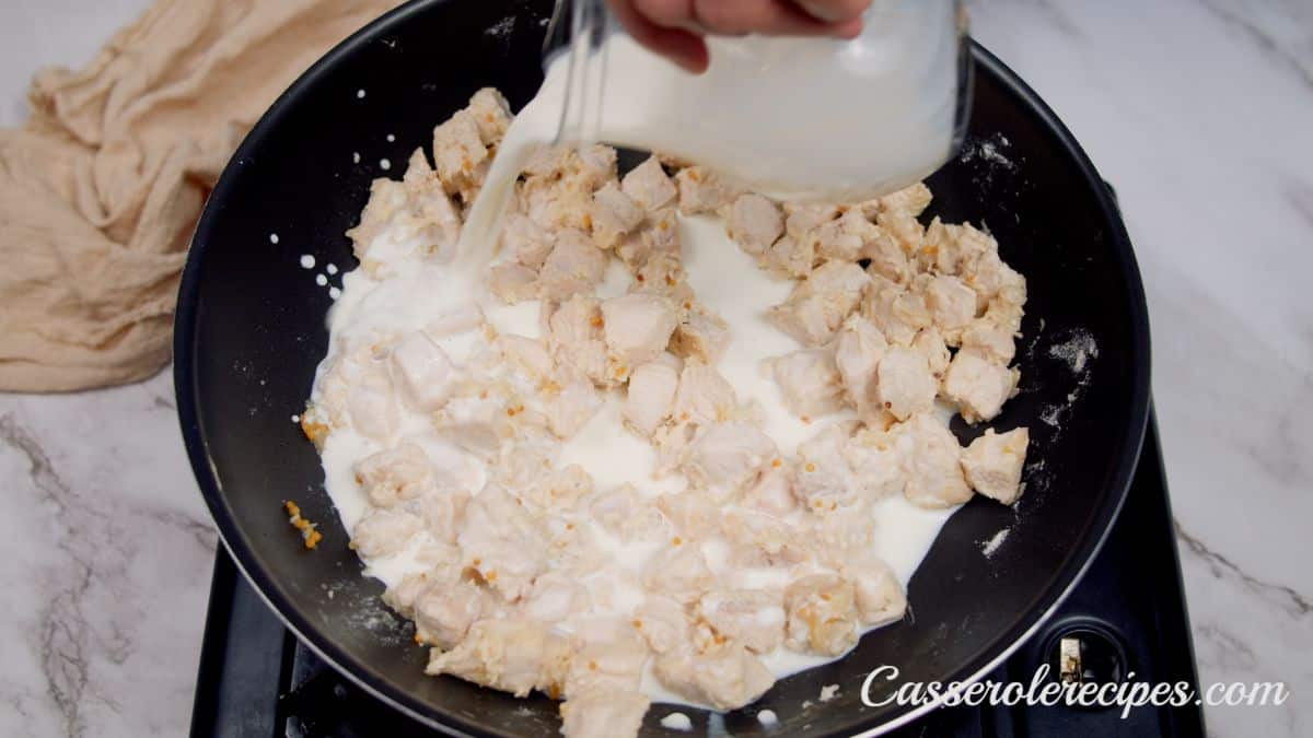 cream being poured over top of cooked chicken in skillet