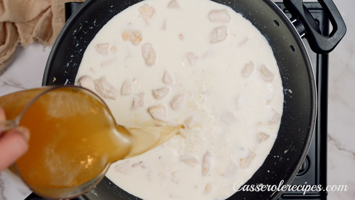 chicken broth being poured into skillet with chicken and cream