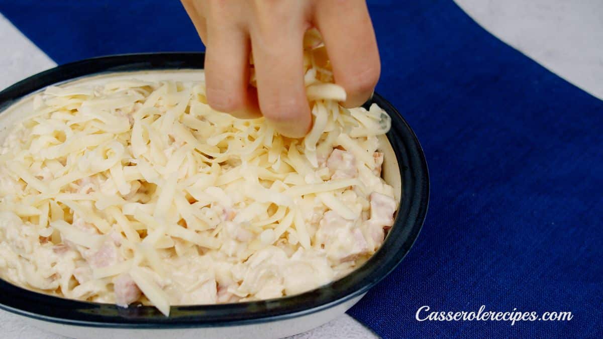 hand sprinkling cheese over top of casserole